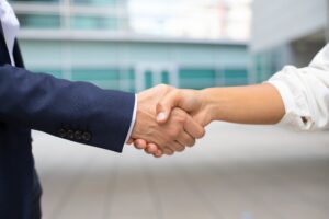 A close-up shot of two people in business suits shaking hands, representing a successful partnership with an Indian top lawyer